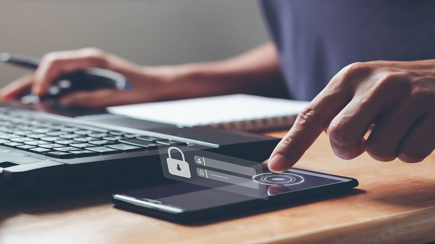 A person using a laptop for online account and verifying their identity on their cell phone using multi-factor authentication.