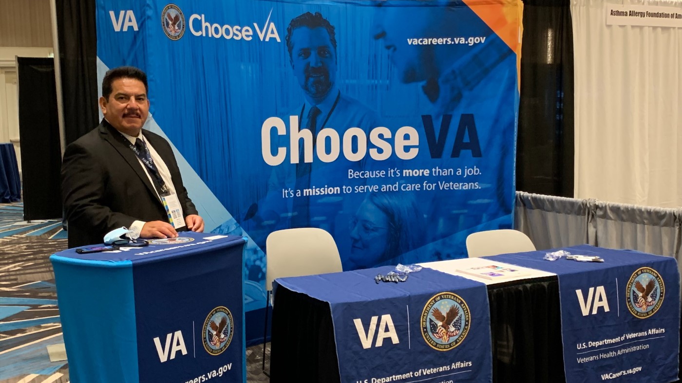A VA recruiter stands at a booth at a national event.