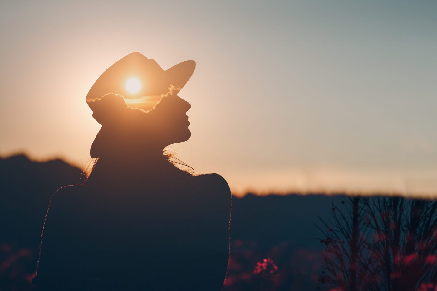 Silhouette of woman in hat gazing at sunset.