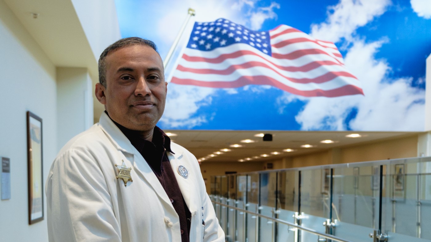 A chief of staff stands in front of an American flag mural in a VA facility.