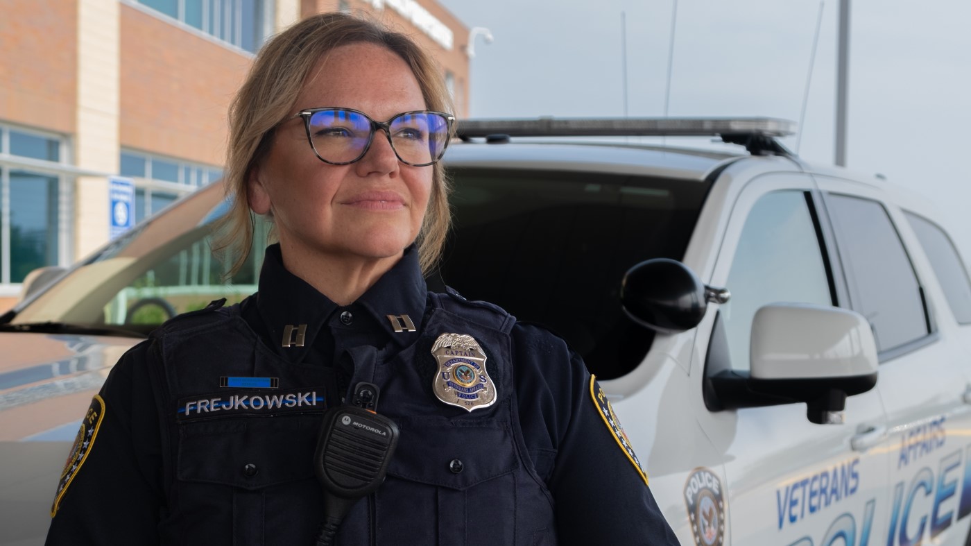 A female VA Police Officer standing outside a facility, posted next to a VA police vehicle.