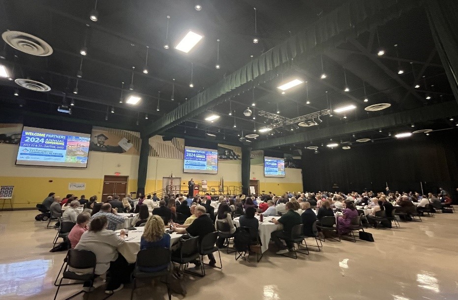 People seated at tabled gathered in a convention space.