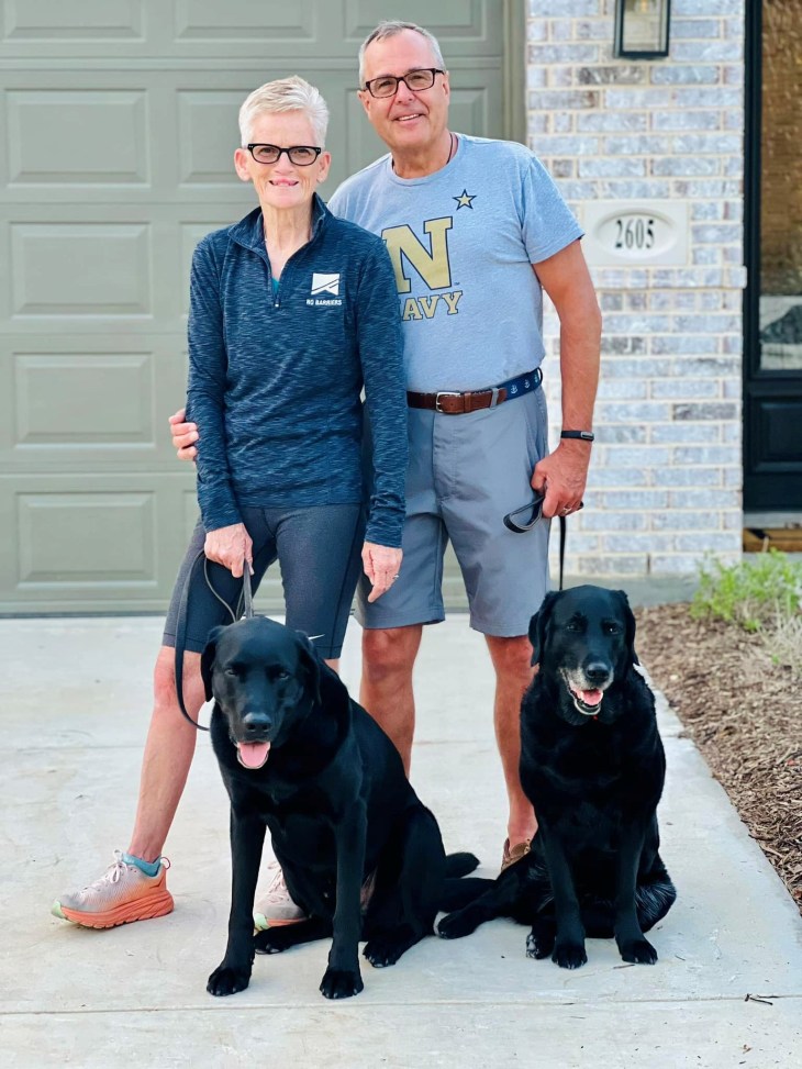 Man and woman standing together with two black dogs.