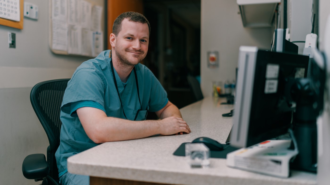 A man in scrubs sits at a computer, enjoying the results of a successful job search that brought him to VA.