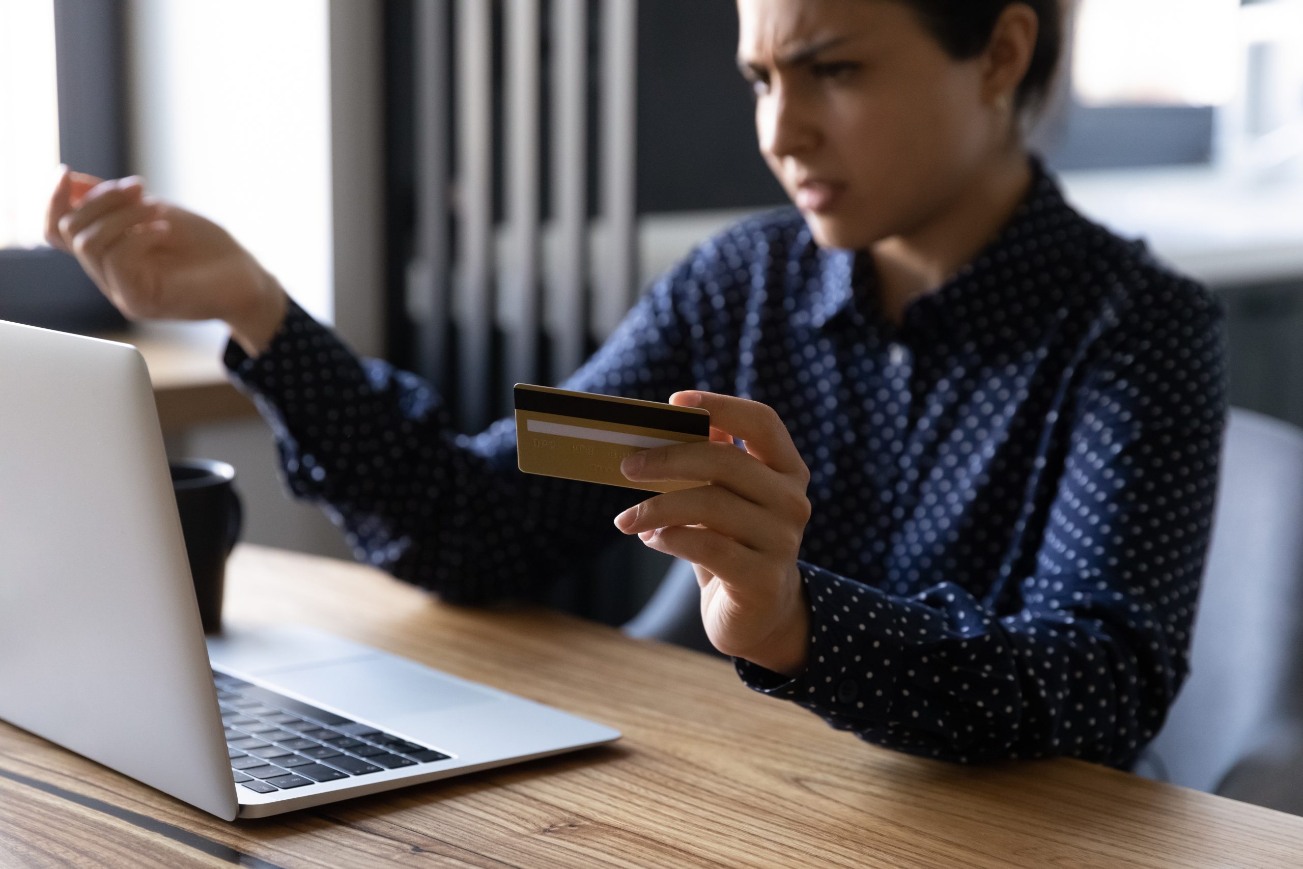 Woman using laptop and holding credit card with a look of frustration.